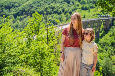Karadağ. Anne ve oğul turistler Tara Nehri üzerindeki Dzhurdzhevich Köprüsü 'nün arka planında. Karadağ 'da seyahat etmek. Karadağ manzarası.