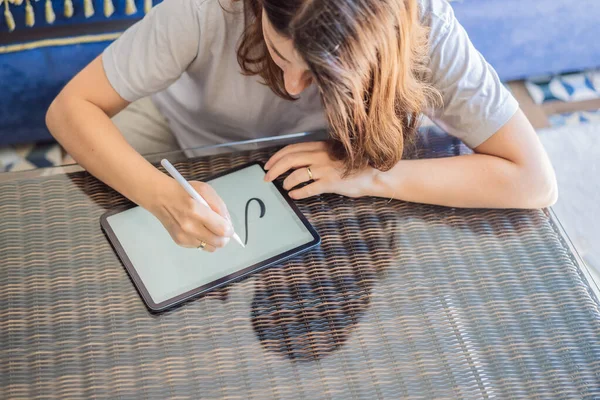 Calligrapher Young Woman writes phrase on digital tablet. Inscribing ornamental decorated letters. Calligraphy, graphic design, lettering, handwriting, creation.