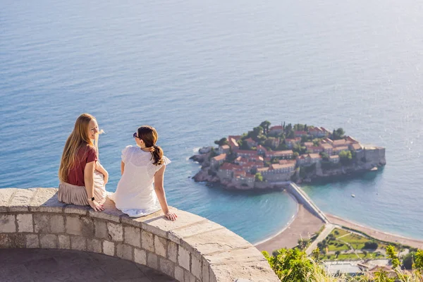 Two Woman tourist on background of beautiful view of the island of St. Stephen, Sveti Stefan on the Budva Riviera, Budva, Montenegro. Travel to Montenegro concept.