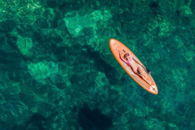 Genç kadınlar, Karadağ 'ın mavi sularında ayakta kürek çekerken eğleniyorlar. - Süper. Kayaların yanındaki sörf tahtasındaki kız eğitimi..