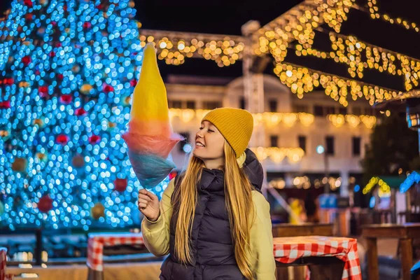 若い女性を保持綿キャンディーと笑顔でクリスマスフェア身に着けています黄色のウールキャップ — ストック写真