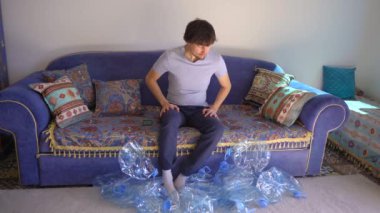 Genç bir adam boş plastik şişelerle çevrili bir kanepede oturuyor. Telefonunda tüm bu plastikleri götürebileceği bir yer arıyor..