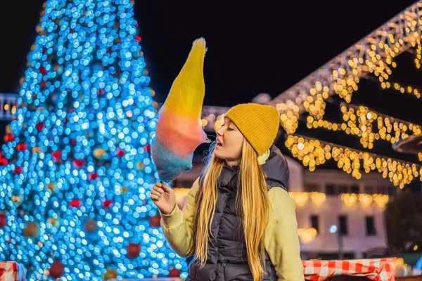 若い女性を保持綿キャンディーと笑顔でクリスマスフェア身に着けています黄色のウールキャップ — ストック写真