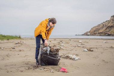 Plastik çöp. Deniz ve okyanus kirliliği. Plaj temizliği. Genç adam kumsalda kullanılmış plastik şişe topluyor. Çevreci aktivist çöp topluyor. Dünyamızı kurtar. Doğa koruması.