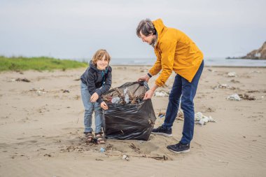 Plajı temizleyen eldivenli baba ve oğul kirli denizi temizleyen plastik torbaları topluyorlar. Çocukların doğal eğitimi. İnsan yapımı kumsalda dökülen çöplerle ilgili bir sorun..