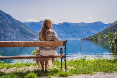 Bir kadın bankta oturuyor ve Kotor Körfezi manzarasına hayran. Karadağ.