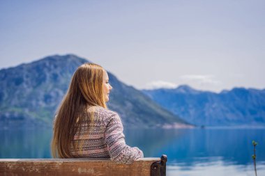 Bir kadın bankta oturuyor ve Kotor Körfezi manzarasına hayran. Karadağ.