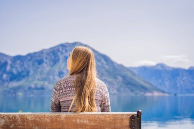 Bir kadın bankta oturuyor ve Kotor Körfezi manzarasına hayran. Karadağ.