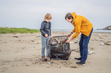 Plajı temizleyen eldivenli baba ve oğul kirli denizi temizleyen plastik torbaları topluyorlar. Çocukların doğal eğitimi. İnsan yapımı kumsalda dökülen çöplerle ilgili bir sorun..