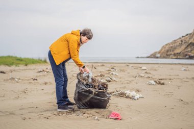 Plastik çöp. Deniz ve okyanus kirliliği. Plaj temizliği. Genç adam kumsalda kullanılmış plastik şişe topluyor. Çevreci aktivist çöp topluyor. Dünyamızı kurtar. Doğa koruması.