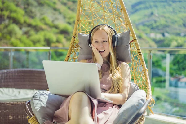 Caucasian woman sitting on the terrace working from home using computer laptop. Young woman teaches a foreign language or learns a foreign language on the Internet on her balcony. Online language