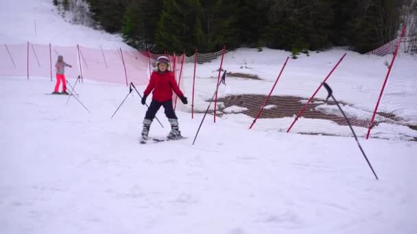 一个穿着红色夹克的小男孩正在学习滑雪 他沿着训练跑道骑着马 试图绕着老师布置的木棍转 — 图库视频影像