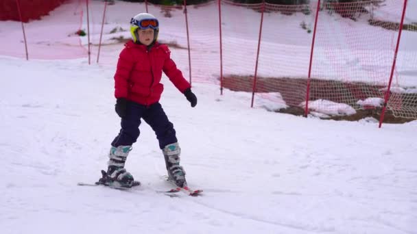 赤いジャケットを着た少年がスキーの仕方を学んでいる 彼は坂を下っている — ストック動画