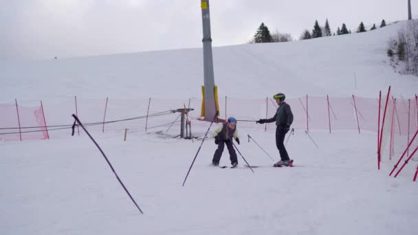 若い女性はプロのスキーインストラクターの監督の下でスキーを学ぶことです 彼女は教師によって配置された棒の周りにジグザグにしようとするトレーニングトラックを下ります — ストック動画