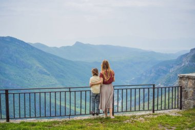 Mavi nehrin arka planında yeşil vadiden uzak dağlara doğru koşan anne ve oğul turistler. Karadağ 'ın güzel dağları ve Cievna Nehri.