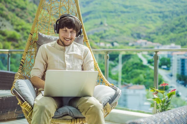 Handsome caucasian man sitting on the terrace working from home using computer laptop. Young man teaches a foreign language or learns a foreign language on the Internet on his balcony. Online language