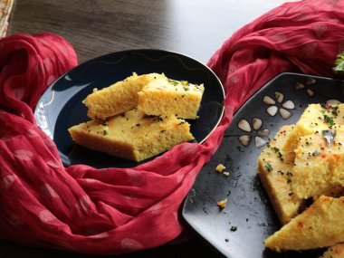 Bir tabak Anında Canlı Dhokla üzerine hardal tohumu dökülmüş corainder yaprakları ve kırmızı biber tozu