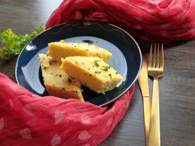 Bir tabak Anında Canlı Dhokla üzerine hardal tohumu dökülmüş corainder yaprakları ve kırmızı biber tozu