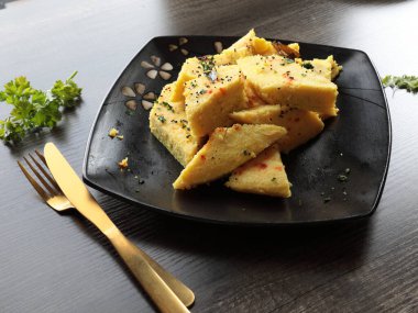 Bir tabak Anında Canlı Dhokla üzerine hardal tohumu dökülmüş corainder yaprakları ve kırmızı biber tozu