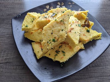 Bir tabak Anında Canlı Dhokla üzerine hardal tohumu dökülmüş corainder yaprakları ve kırmızı biber tozu