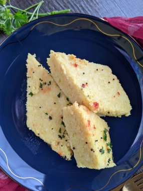 Bir tabak Anında Canlı Dhokla üzerine hardal tohumu dökülmüş corainder yaprakları ve kırmızı biber tozu