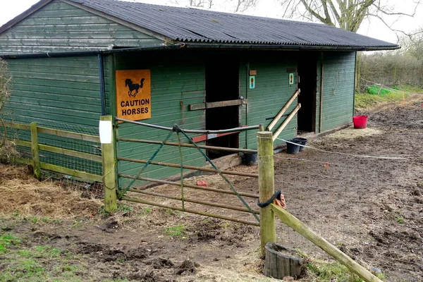 Metal kapının arkasındaki çamurlu arazide at ahırı..