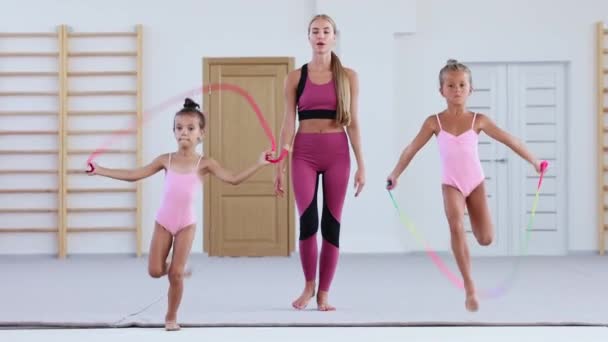 Zwei kleine akrobatische Mädchen, die vorwärts laufen, während sie über das Seil springen und ihre Trainerin beobachtet und verfolgt sie — Stockvideo