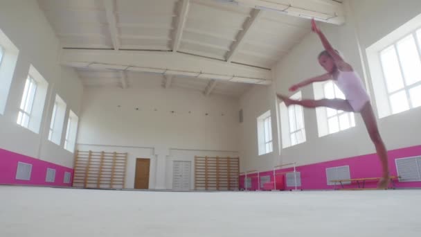 一个表演杂技的小女孩在粉红色的演播室里跳着，双腿展开在空中 — 图库视频影像