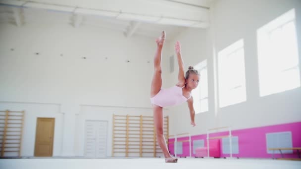 一个杂技表演的小女孩站在体育馆里，把腿伸到头顶 — 图库视频影像