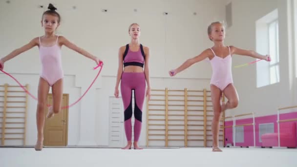 Jimnastik eğitimi - iki küçük akrobatik kız halatın üzerinden atlarken ileri doğru yürüyorlar ve kadın eğitmenleri onları izliyor. — Stok video