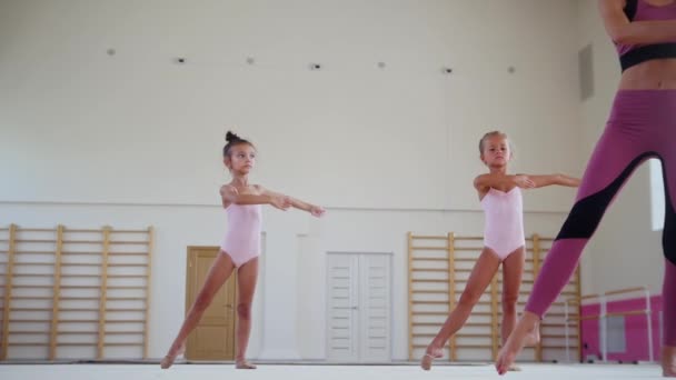 Entrenamiento gimnástico: entrenadora femenina que muestra a sus dos niñas estudiantes movimientos acrobáticos de danza — Vídeos de Stock