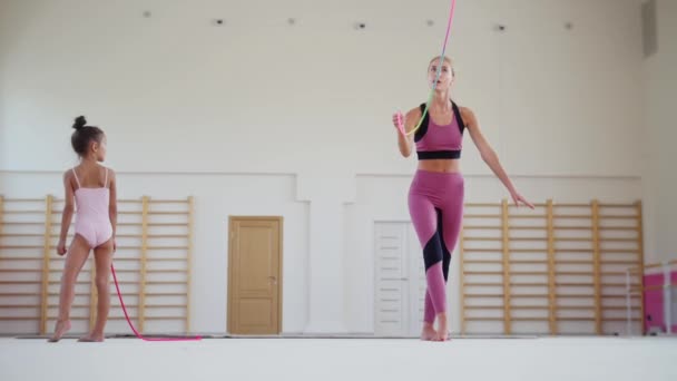 Entraînement gymnastique - formatrice montrant à ses deux petites filles étudiantes comment jouer avec une corde colorée dans la salle de sport — Video