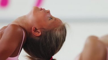 İki küçük kız jimnastikçi, eğitime sırtlarını yaslıyor ve başparmaklarını başlarıyla uzatmaya çalışıyorlar.