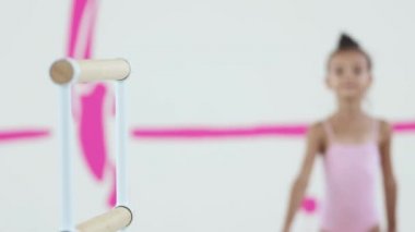 Küçük bir jimnastikçi kız tırabzana doğru yürür ve kameraya bakar.