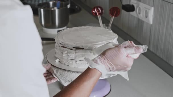 Женщина-повар делает торт - наносит крем на свежий торт из кондитерской сумки — стоковое видео