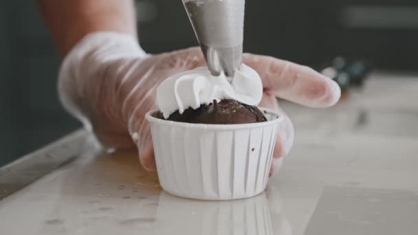 Női szakács alkalmazása fehér krém tetején egy cupcake — Stock videók