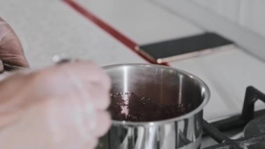 Beyaz mutfaktaki kadın aşçı tencerede kirazla şeker eritiyor.