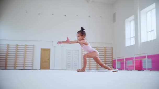 Spor salonunda antrenman yapan küçük bir kız bacağıyla çemberi yukarı fırlatıyor. — Stok video