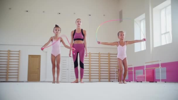 Gymnastik träning - två små akrobatiska flickor hoppar över repet och deras kvinnliga tränare tittar på dem — Stockvideo