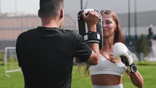 Молодая женщина, занимающаяся боксом со своим тренером мужского пола - удары в перчатки — стоковое видео