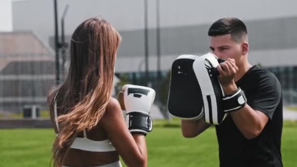 Ung kvinna med långt hår har en boxning utbildning med sin man tränare - stansning i vantar på händerna — Stockvideo