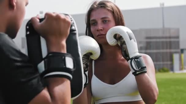 Giovane donna in guanti boxer pugni in guanti sulla mano del suo allenatore maschile — Video Stock