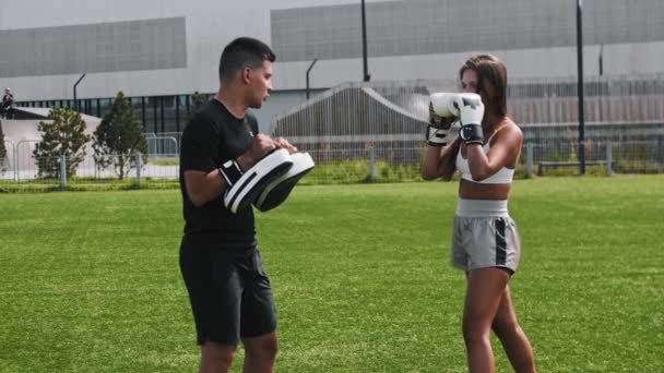 Ung kvinna med boxerhandskar som tränar och sparkar sin tränare i handsken — Stockvideo