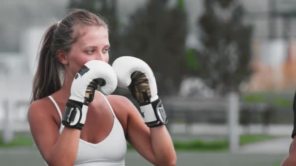 Młoda kobieta w białej bluzce trenuje boks ze swoim trenerem — Wideo stockowe