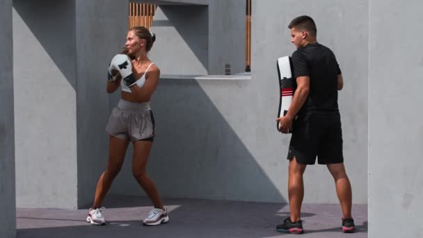Beyazlar içindeki genç kadın dışarıda koçuyla boks antrenmanı yapıyor. — Stok video
