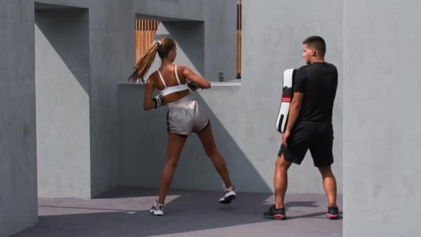 Młoda kobieta w białej bluzce ma trening bokserski z trenerem na zewnątrz - kopie miękkiego obrońcę — Wideo stockowe