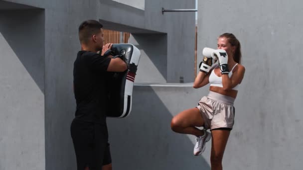 Молода жінка, яка тренується з боксу на відкритому повітрі, штовхає портретний мішок, прикріплений до свого тренера — стокове відео