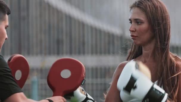 Обучение боксу - молодая женщина с длинными волосами бьет перчатки на руках своего тренера — стоковое видео
