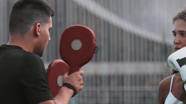 Boksen training - jonge vrouw met lang haar ponsen de handen van haar trainer — Stockvideo