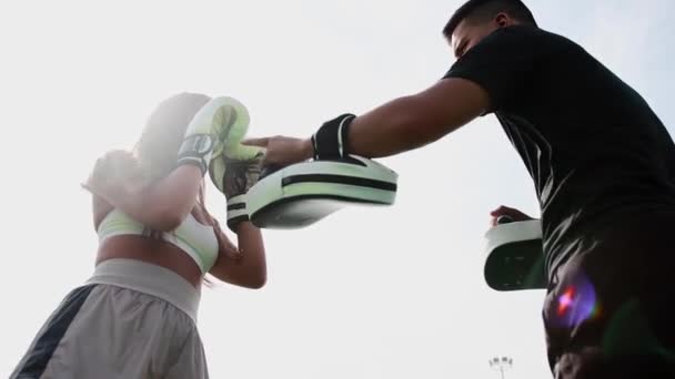 Обучение боксу на свежем воздухе - молодая женщина бьет в лапы на руке тренера — стоковое видео